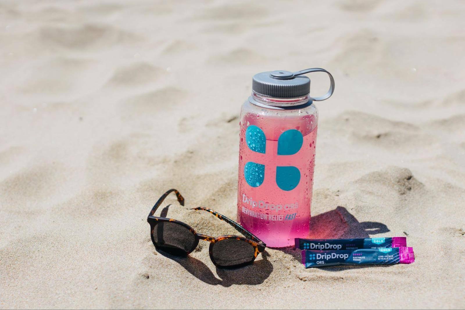 DripDrop ORS tumbler, sachets and sunglasses on the sand
