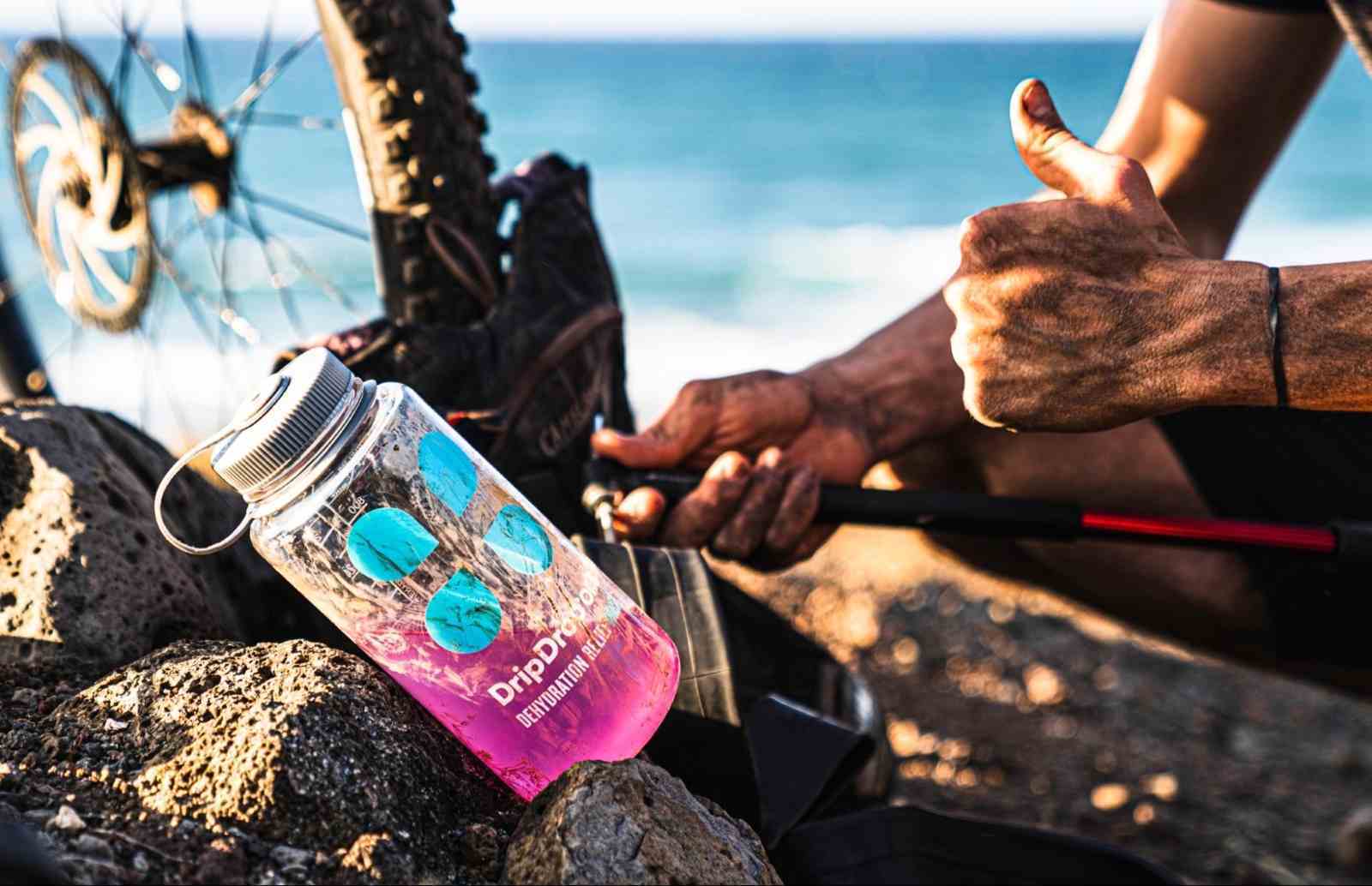how to rehydrate: Tumbler with DripDrop ORS on top of rocks and a biker giving a thumbs up in the background