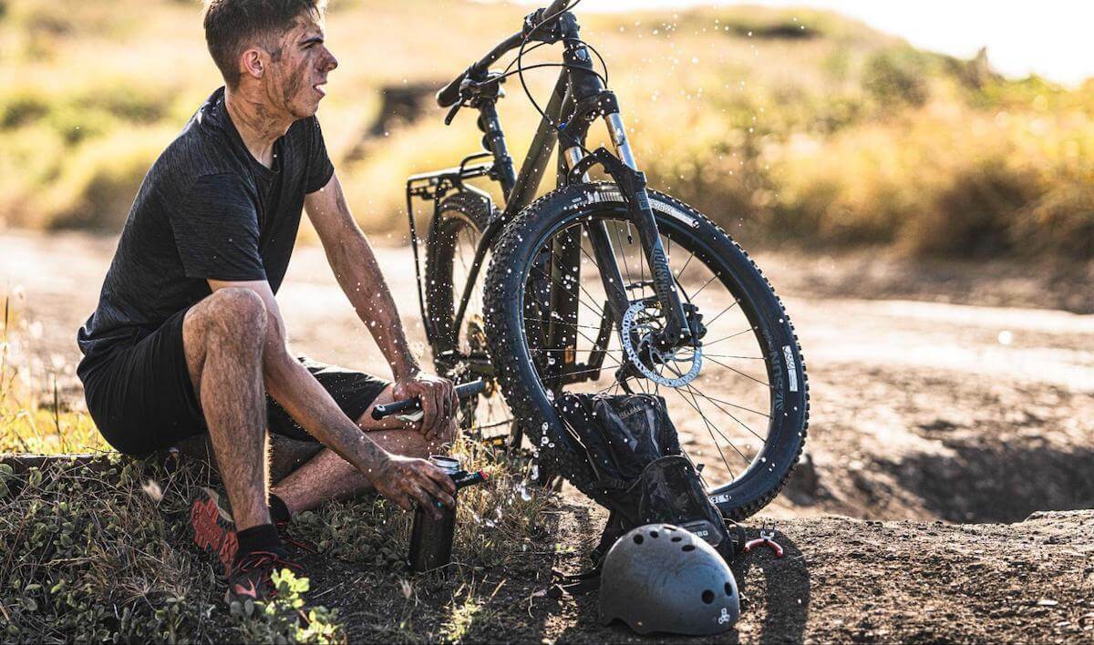 Not drinking enough water: biker holding a sachet of DripDrop while sitting beside his bike
