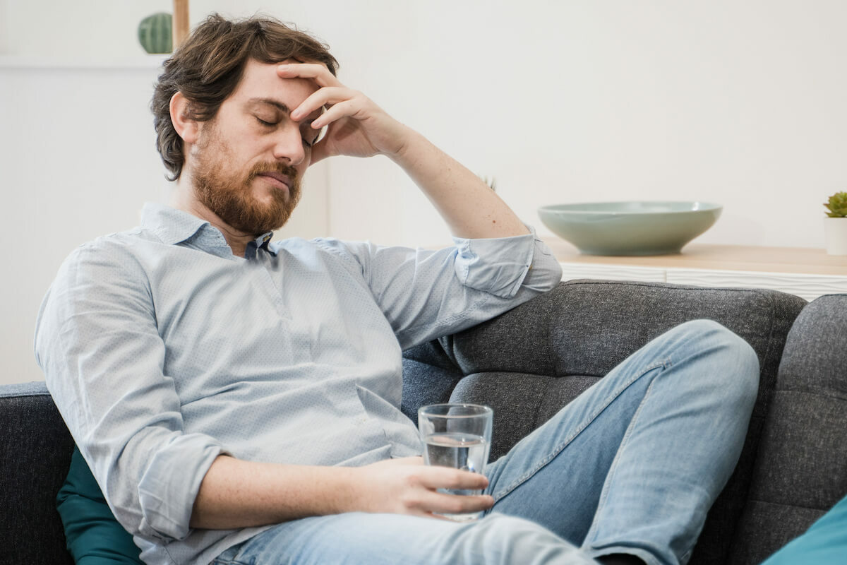 What does a dehydration headache feel like: man with a headache holding a glass of water