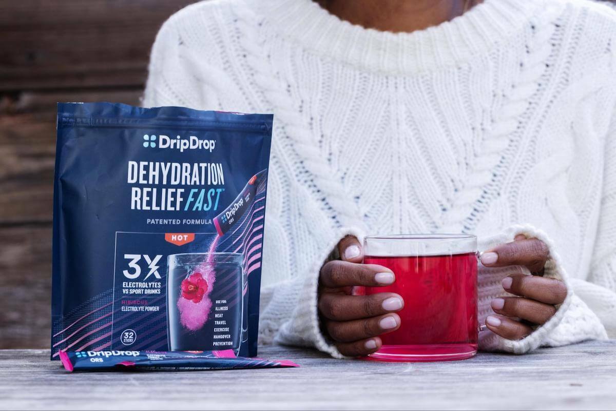 Person holding a glass of DripDrop ORS and a pack of DripDrop pack